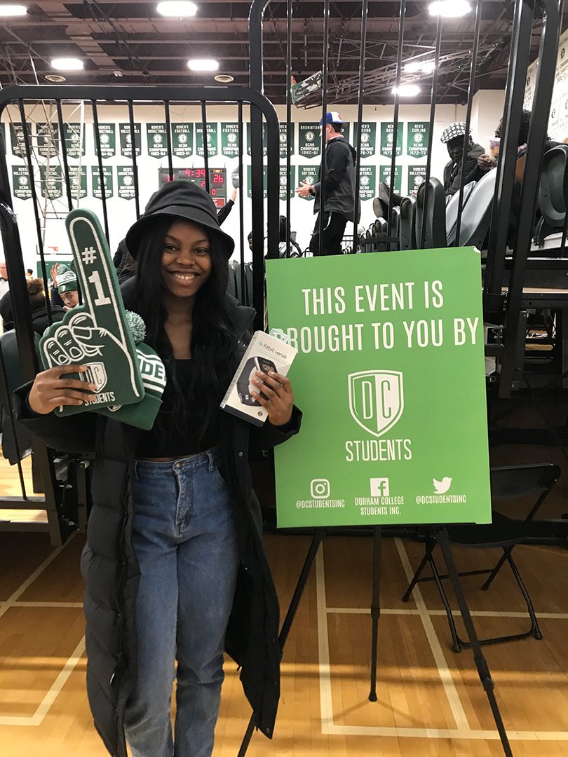 A student holding a DCSI foam finger and hat beside a green DCSI sign.