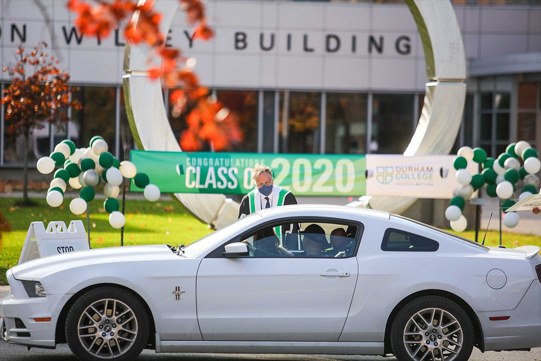 2020 Spring Convocation graduate drives by to receive materials from a DC staff member.