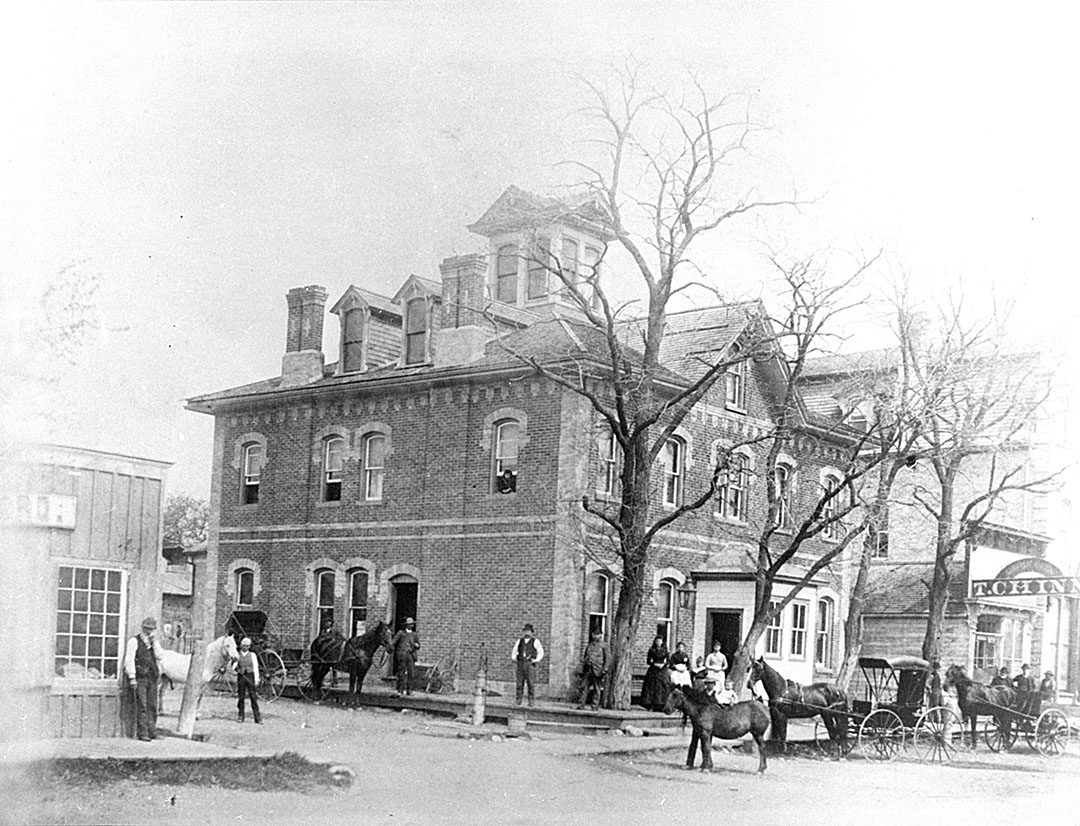 BROOKLIN, Ont., 1892 – The Brooklin Hotel. There are several people standing in front of the hotel and horses and horse-drawn carts.