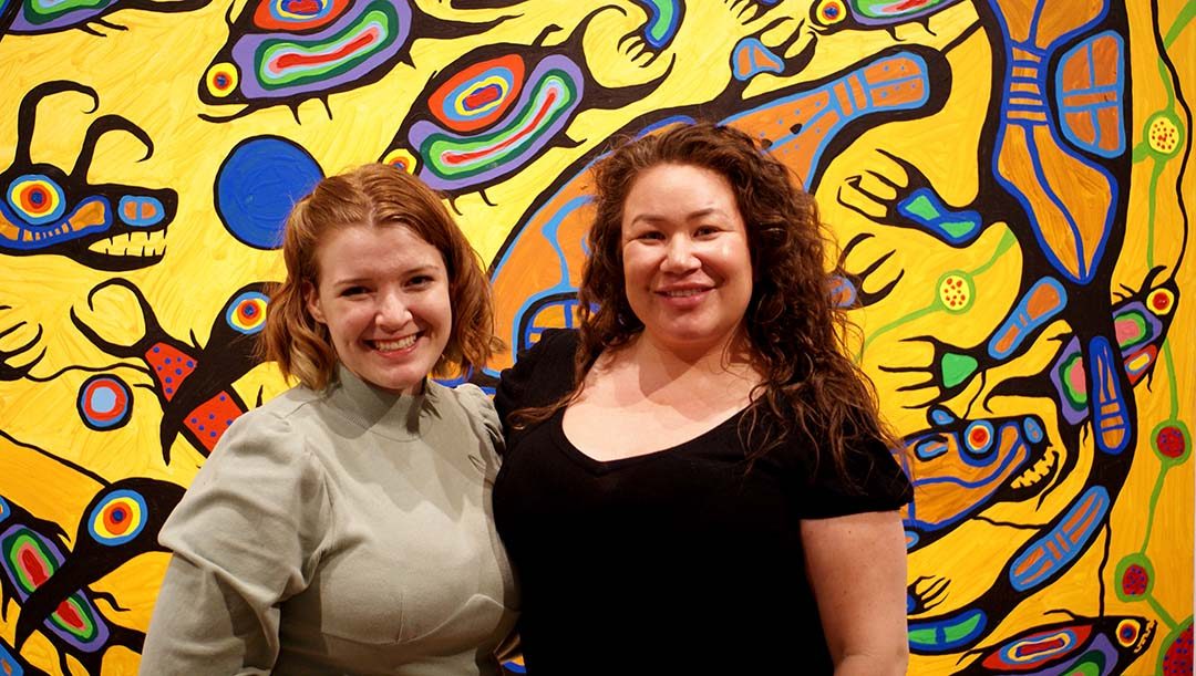 Liz Morris, student network and engagement coordinator with the DCSA (left), and Amanda Banning, student success coordinator at FPIC, pose in front of an Indigenous painting at the Robert McLaughlin Gallery.