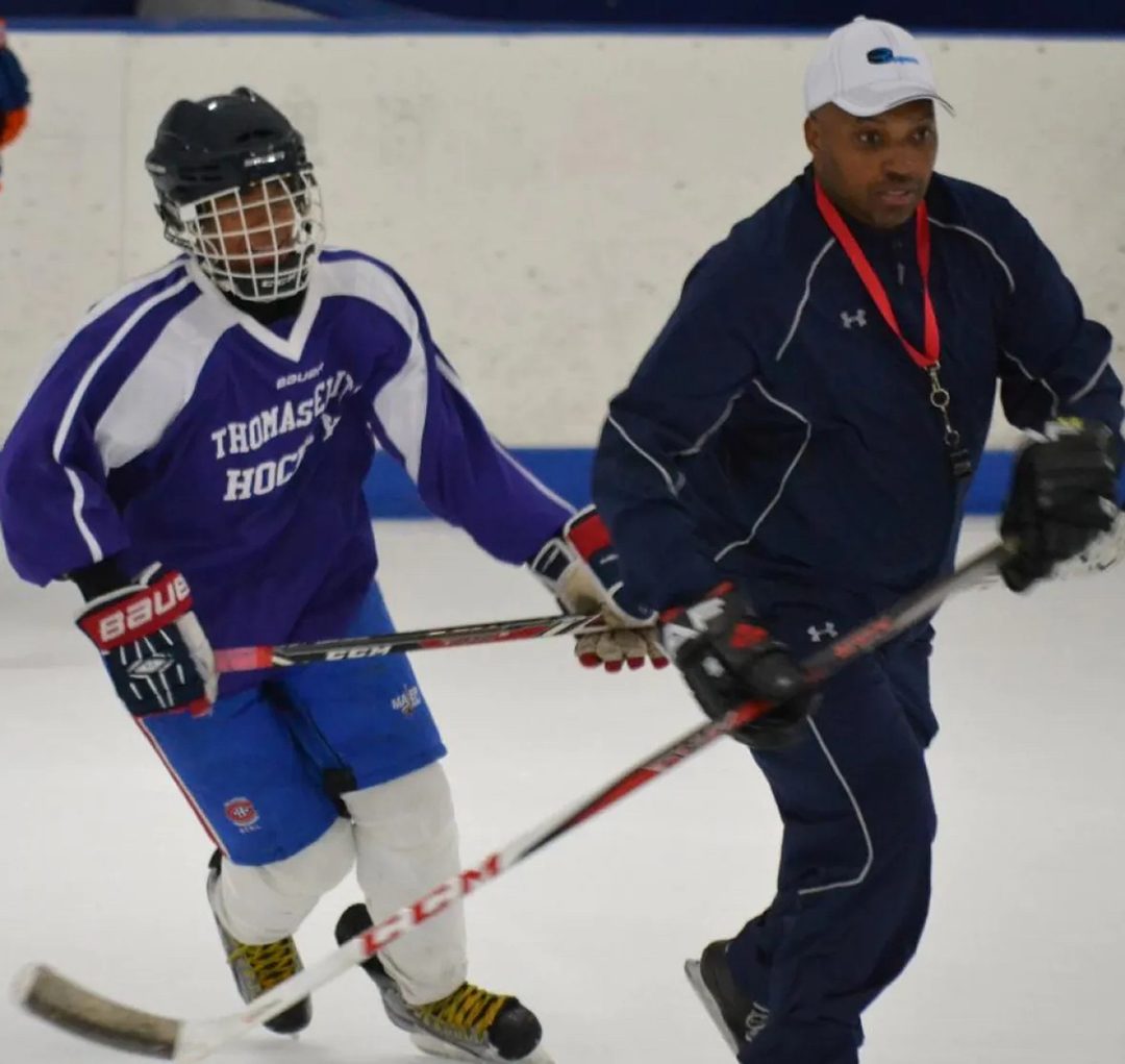 Black hockey coach, Cyril Bollers, skating with a Black player in a practice.