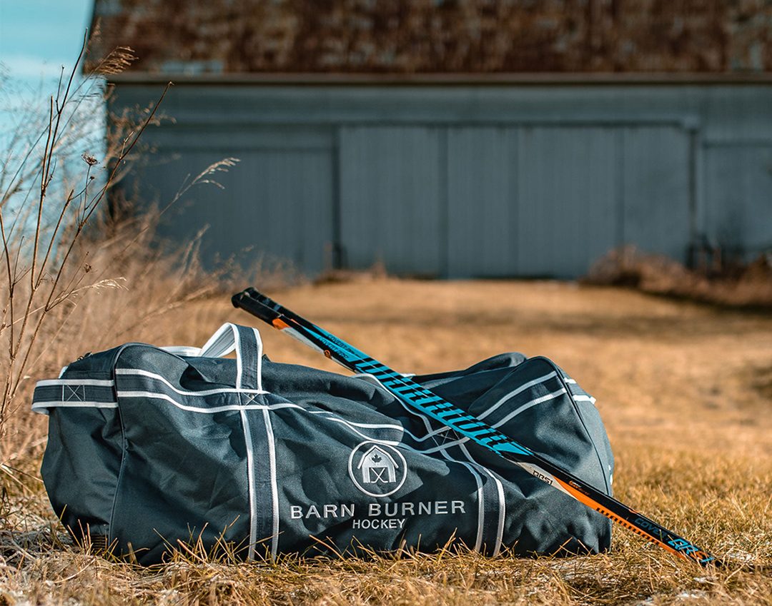 A hockey bag sitting outside in wheat on farmland.