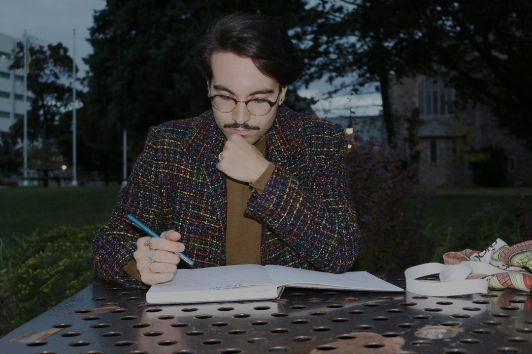 Justin Mezzapelli sits at a table writing in his notebook.