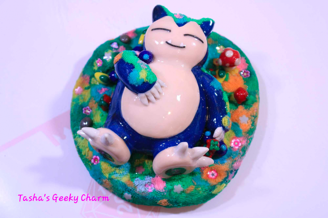 A handmade Snorlax from Pokemon with one arm on his belly as he takes a nap in a clay circle that looks like flowers and mushrooms.