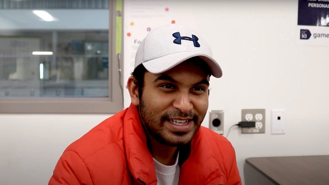 A smiling man wearing a red jacket, white shirt, and white sports brand hat.