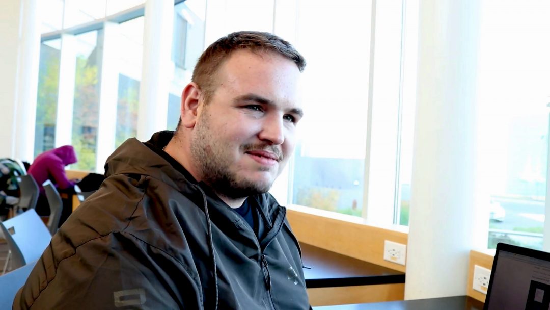 A man with a soft smile. He is wearing a brown-grey windbreaker jacket.