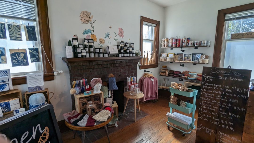 Inside The Collective Market, handcrafted items including clothing and mugs are on display. The hot beverage prices are displayed on the black board to the right.