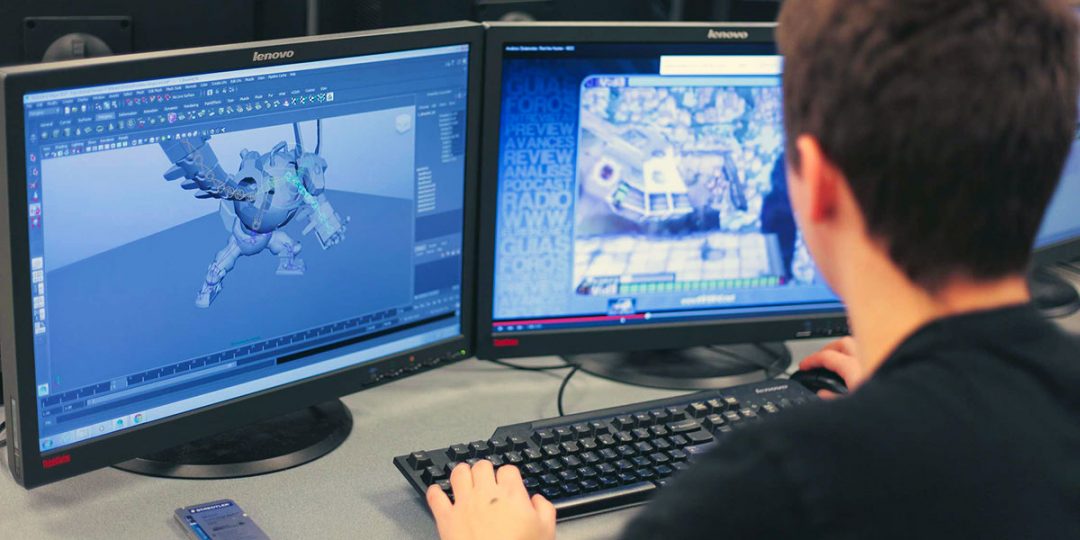 A student sits at a computer desk In front of him are two monitors, a computer mouse, and a computer keyboard. On the monitor to the left, a software for 3D modelling is displayed. On the monitor to the right, a youtube video about video game is being watched.