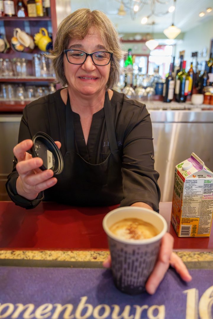 A woman serves a takeaway coffee drink over the counter at the NIce Bistro restaurant in Whitby, Ont.
