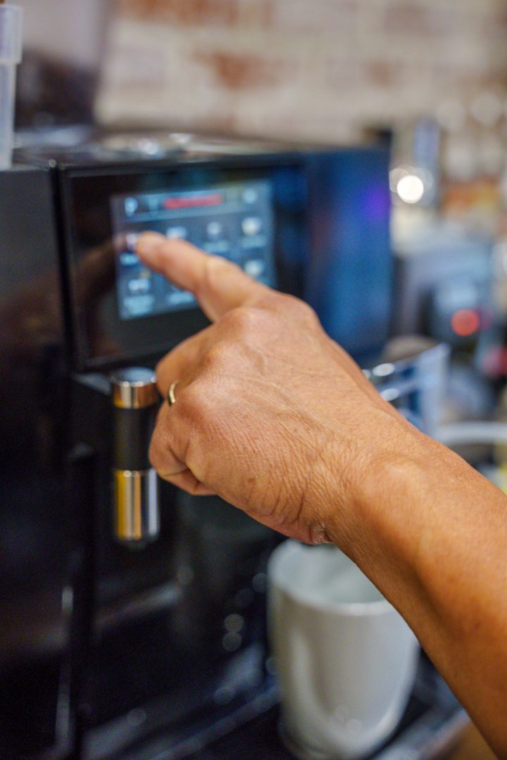 A man presses a digital display on an automatic espresso machine to begin brewing coffee.