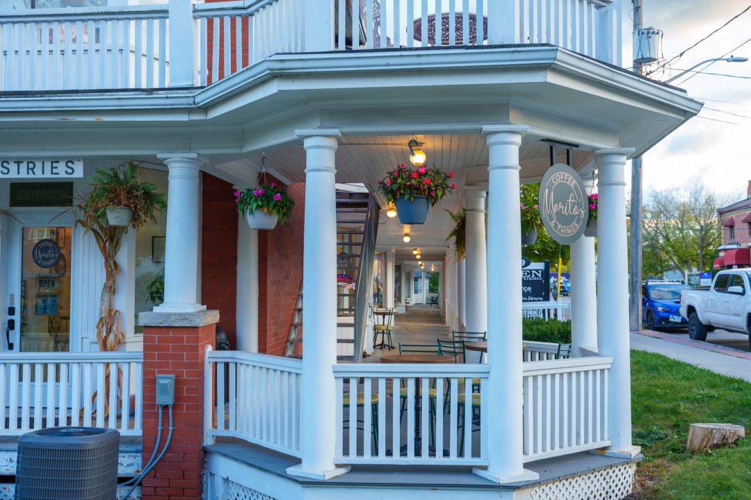 A patio seating area for Marito's Coffee and Things café is located in a hexagonal deck area, surrounded by white pillars and white railings on the corner the shop's larger red brick building.