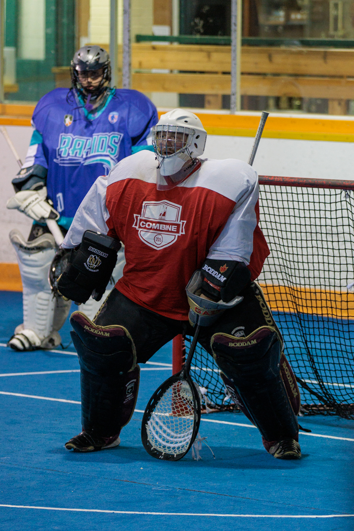 A player wearing goalie gear stands in front of a lacrosse net.