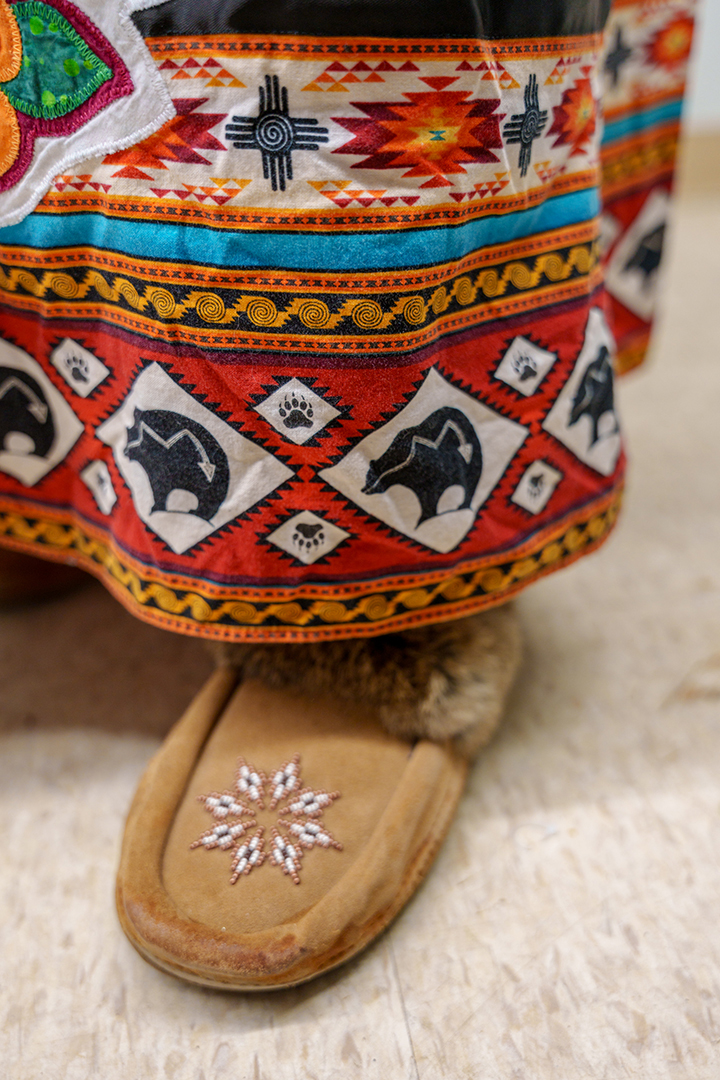 A close-up photo of a woman wearing a traditional Mi’kmaq ribbon skirt and moccasins.