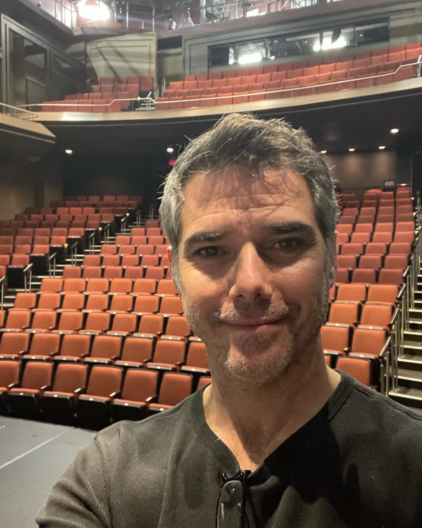 Man stands Infront of a large auditorium with a smile showing how large the theatre is.