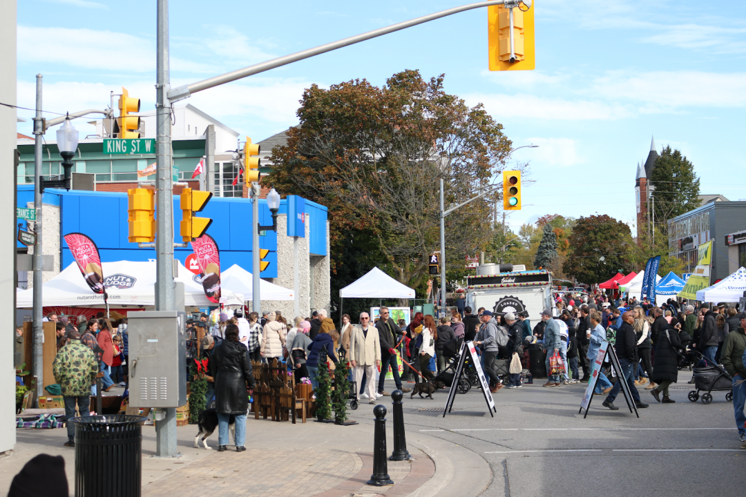 A large crowd of people among vendor tents, all located around an intersection.