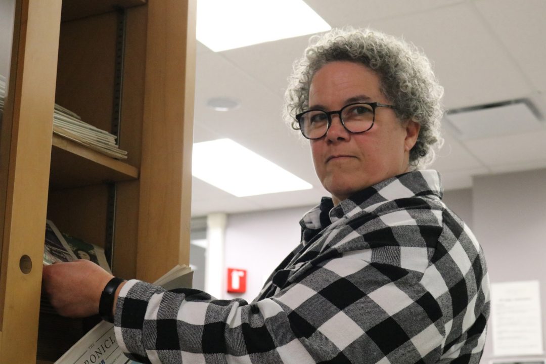 Amy Barron reaching into a cupboard and is grabbing some newspaper in The Chronicle Newsroom. She looks back at the camera with a look of intrigue.