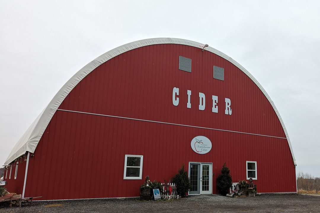 Big red barn with a white roof. Giant letters read "cider" in all capital letters to be easily seen by drivers on the road and other passersby.

A sign hangs above the door that says Geissberger Farmhouse Cider. 

To either side of the store entrance that lays directly in the center of the building, are Christmas decorations.