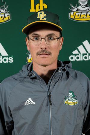 Colin Dempster stands for a headshot behind the Durham College headshot background wearing a Durham College baseball cap and a silver Durham College windbreaker.