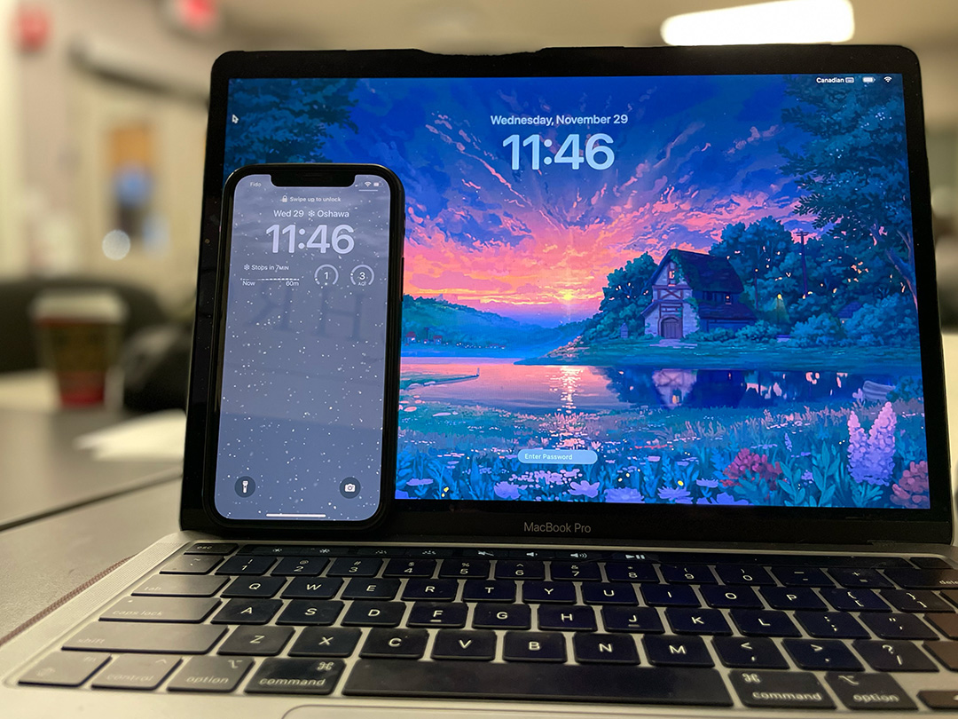 A student's phone sits in front of their MacBook in a classroom.