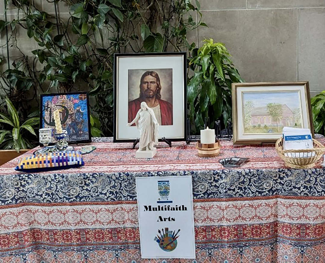 A table covered in a blue, white and red tablecloth. A picture of Jesus, as well as a statue of Jesus, paintings and a candle sit on top.