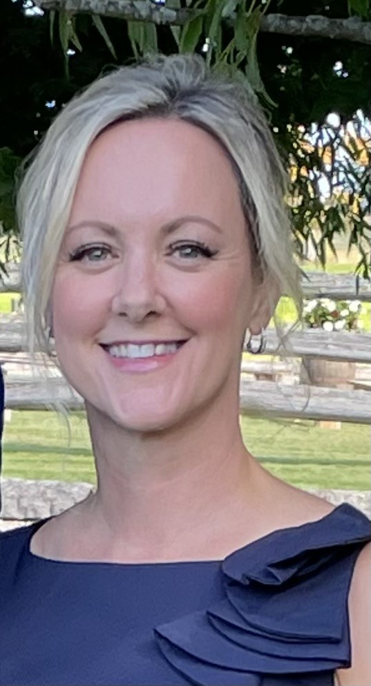 A woman in a blue blouse smiles at the camera.