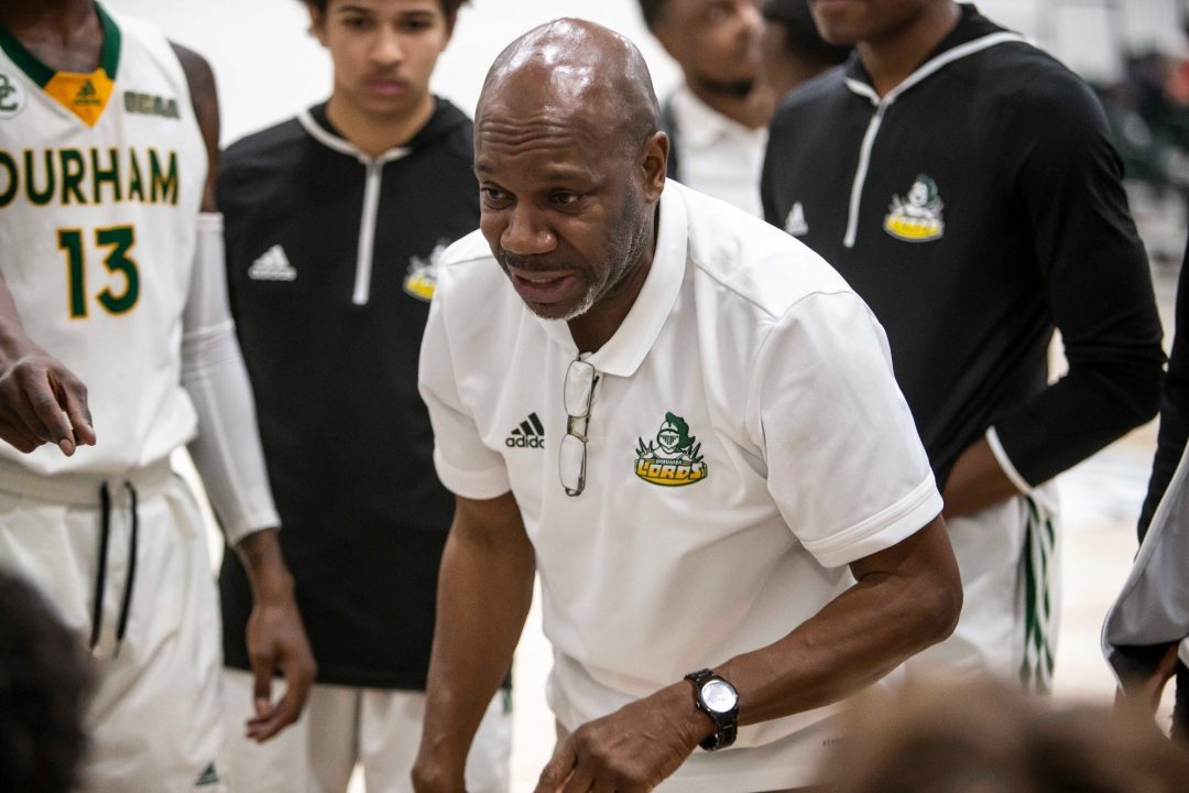 A man in a white shirt speaks to a group of basketball players.