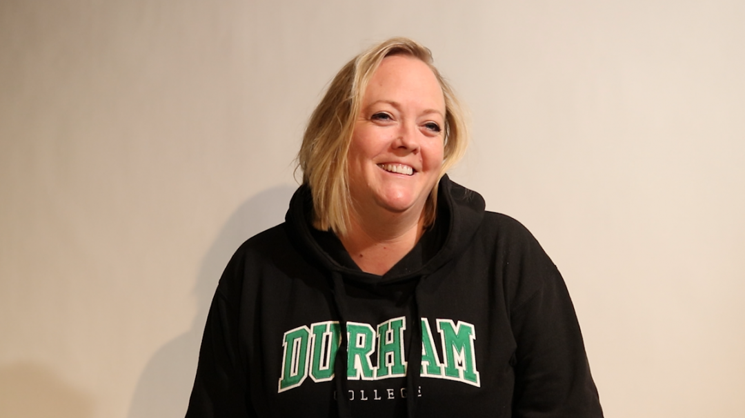 A woman wearing black hoodie with the words Durham College smiles at the camera.