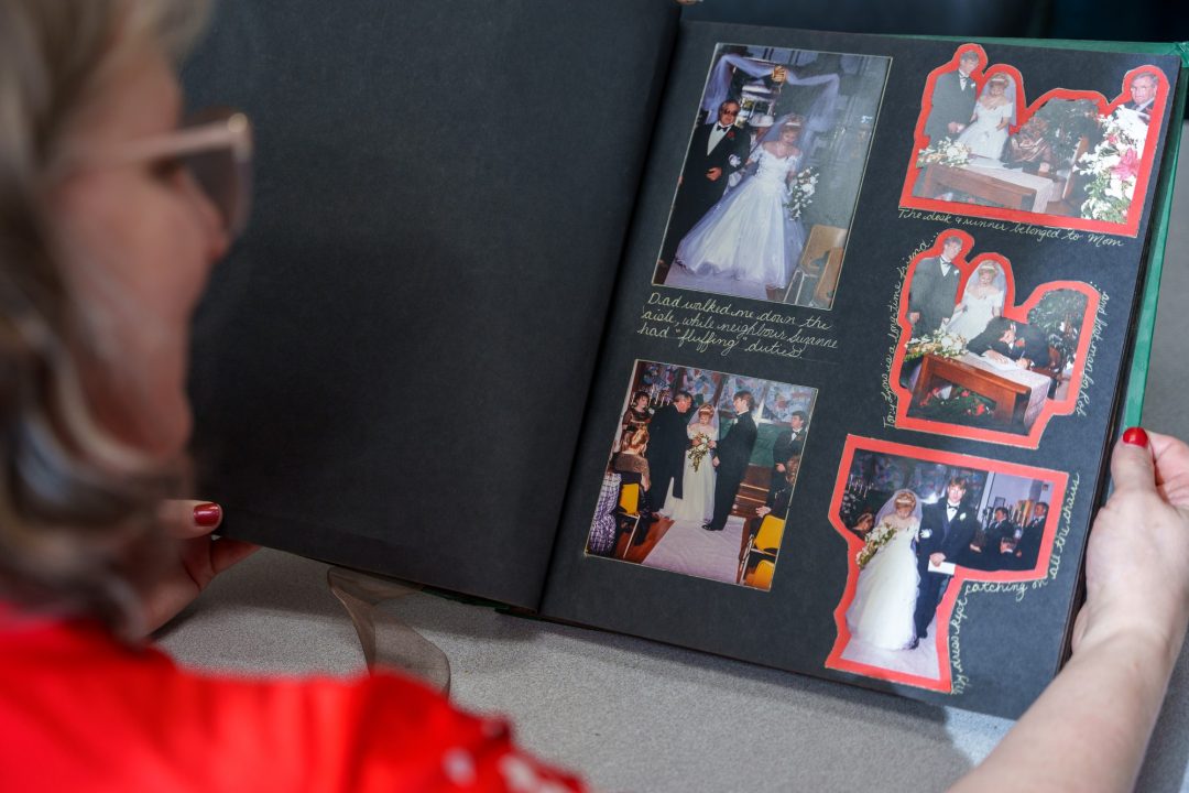 An over-the-shoulder photo of a woman in a red top looking at a scrapbook of her wedding photos.
