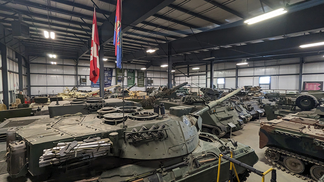 An overhead view from the top of a tank in the hanger at the Ontario Regiment Museum in Oshawa, Ontario. Multiple tanks and military vehicles can be seen. From one Tank, Canadian flags dangle.