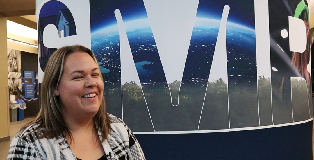 Jesara Holla in front of a sign that says 'SMR' at the OPG visitor centre in Courtice, Ont. on Nov. 19, 2024.