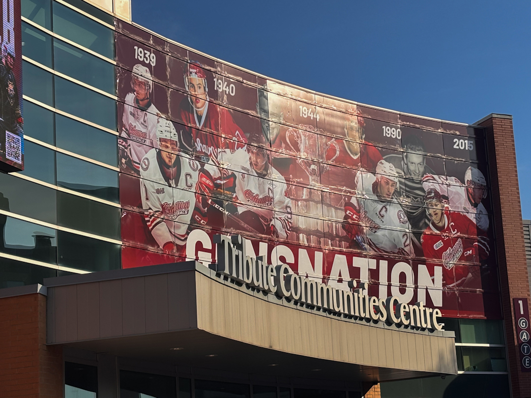 The outside of a building with a large mural featuring the faces of several hockey players. The building sign says "Tribute Communities Centre."