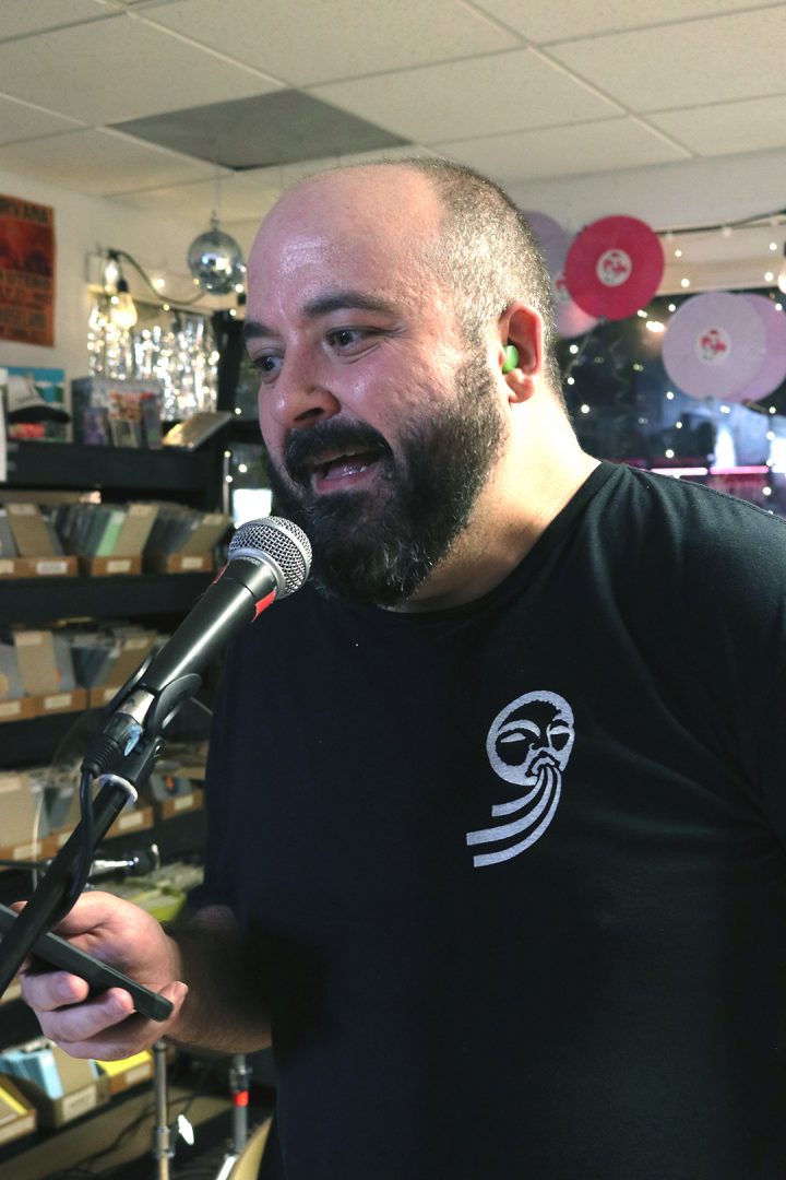 A close-cropped photo of a man with a beard speaking into a mic.