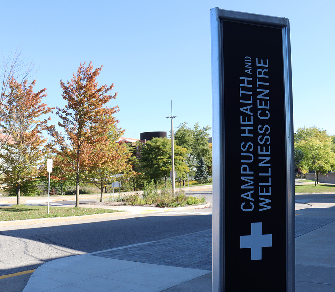 A black sign in a parking lot that reads "Campus Health and Wellness Centre.