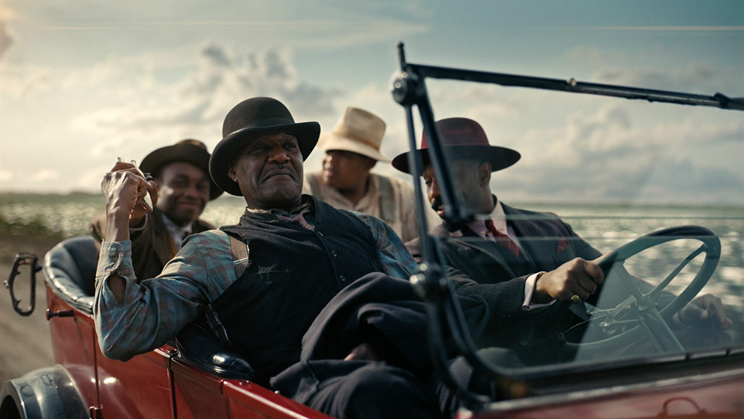 Image of characters Delta Slim, Sammie, Stack, and Cornbread passing around a cigarette while driving down a road.