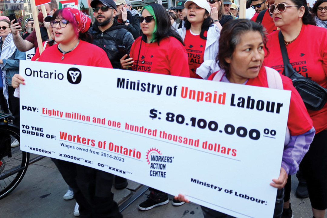 Several women, of different ages, all in red shirts, hold a big cheque during a march.