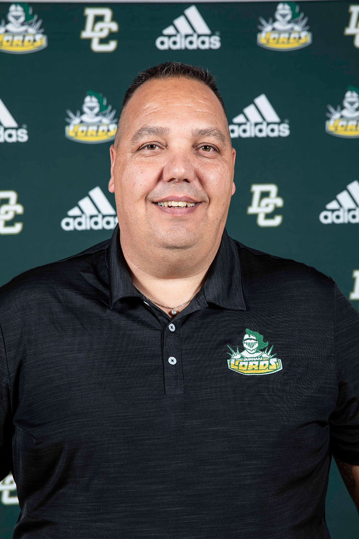 A man smiles for a photo in front of a Durham Lords/Adidas sign.