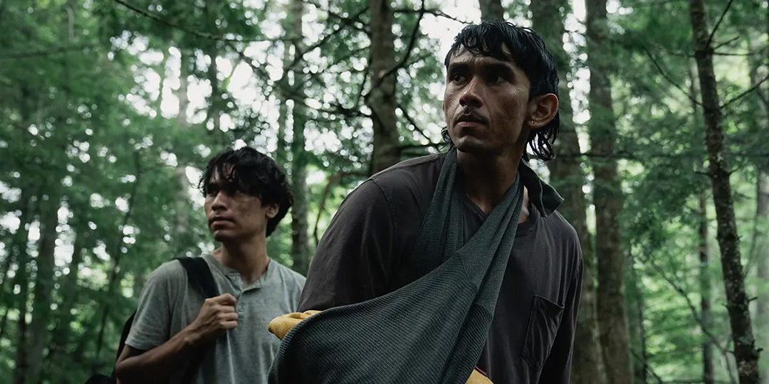 Two Indigenous men walk as they are stranded in the woods.