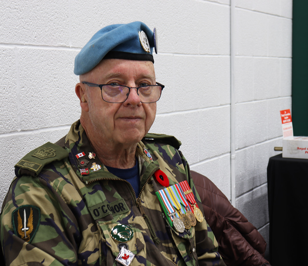 A man with glasses wearing military fatigues and a United Nations beret poses for a photo.