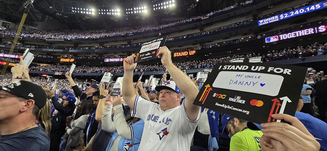 A large crowd in a stadium stands holding signs that say "I stand up for" with a fill-in-the-blank.