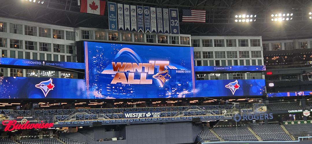 A large sign at the Toronto Blue Jays&squot; World Series game reads "Want it all" in gold on a blue background, featuring the Blue Jays&squot; symbol.