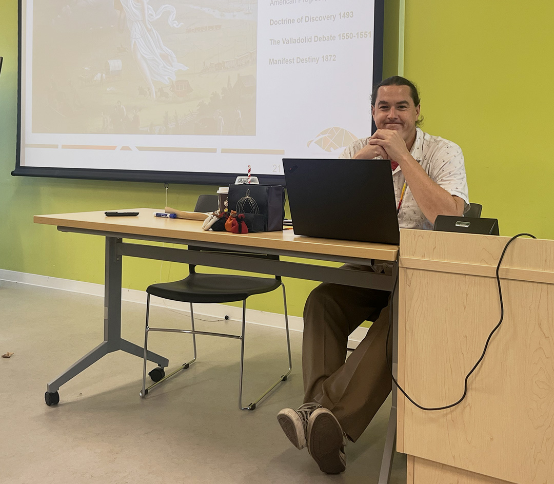 A man sits at a desk smiling at the camera.