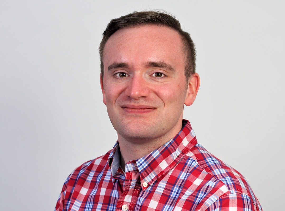 A headshot photograph of a man looking at the camera and smiling, pictured against a white background