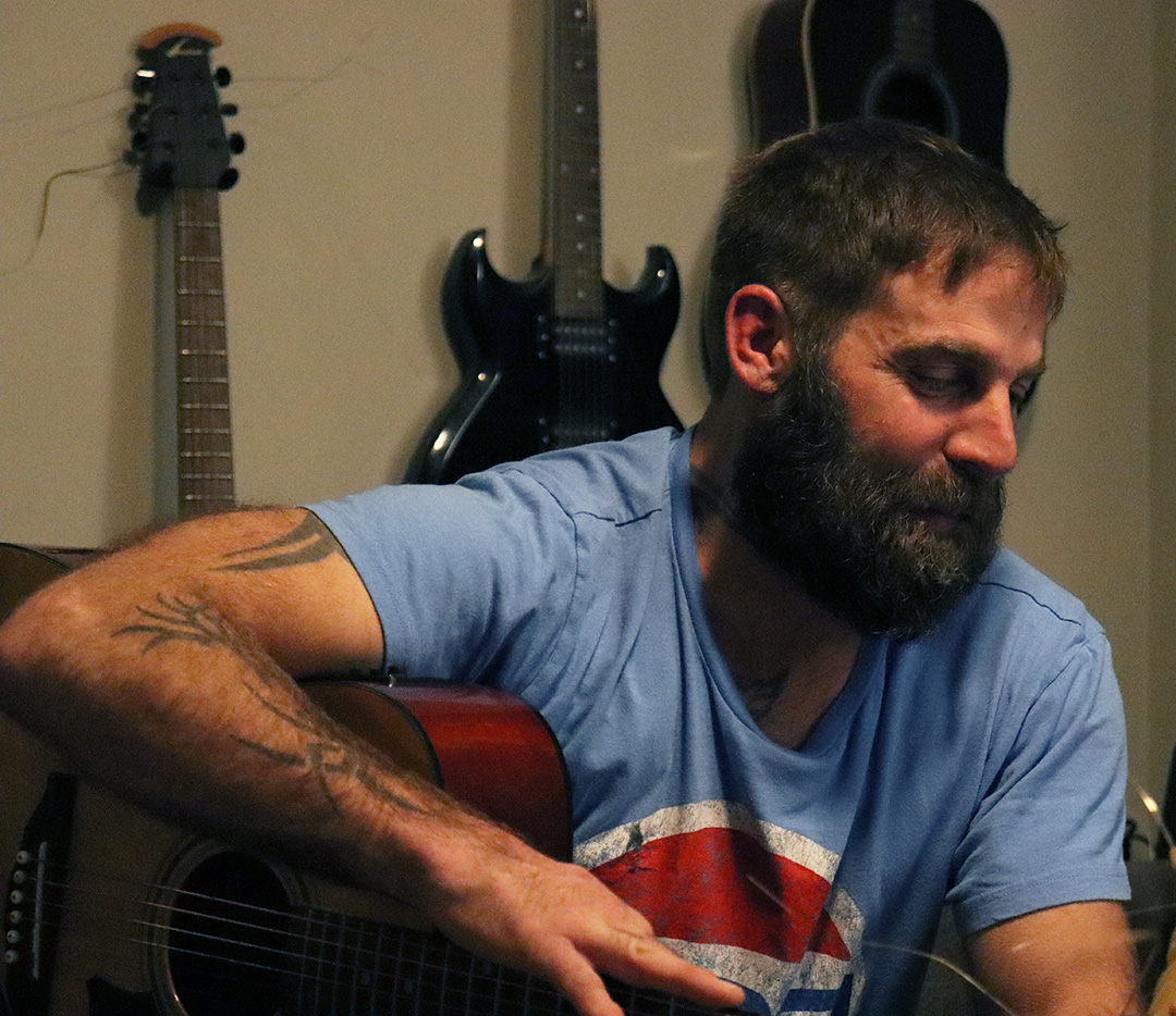 A man in a blue shirt is holding a guitar.