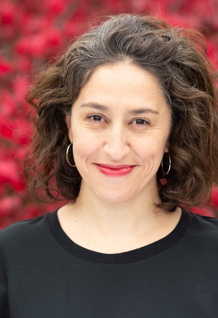 A woman with neck-length hair looks at the camera and smiles, pictured against an out-of-focus red background