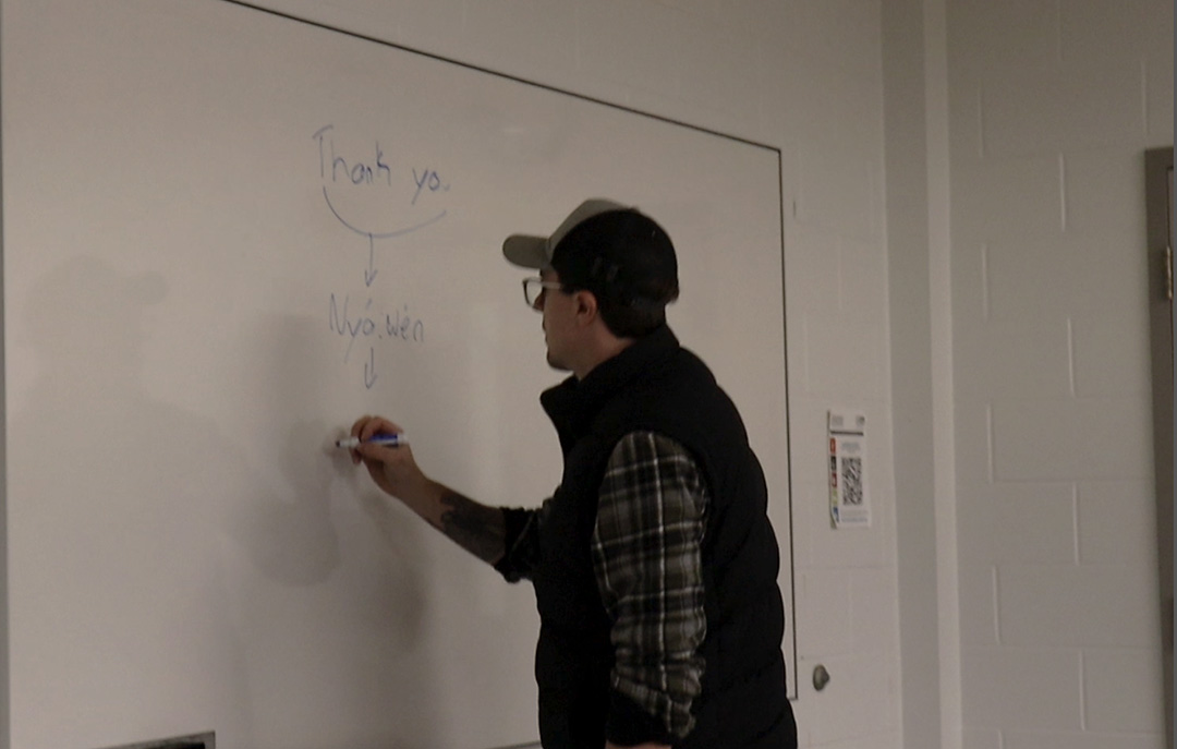 A man stands at a whiteboard writing words in Mohawk.