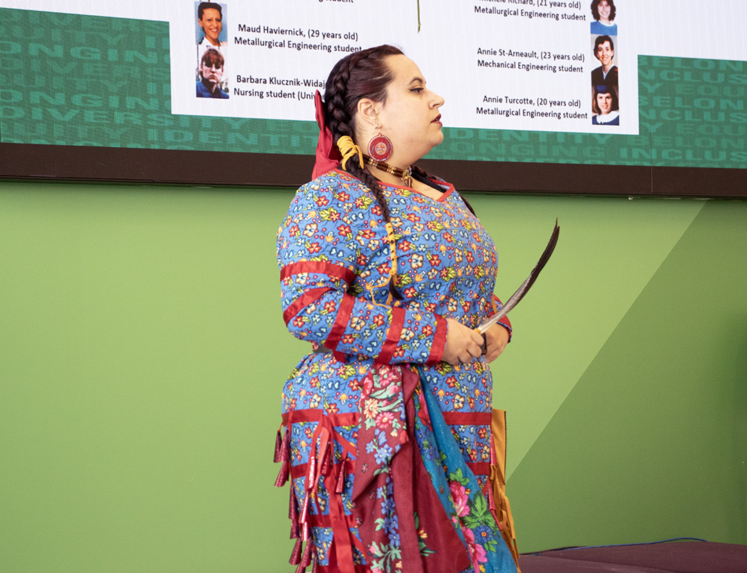 A woman dances in Indigenous regalia, holding an eagle feather.
