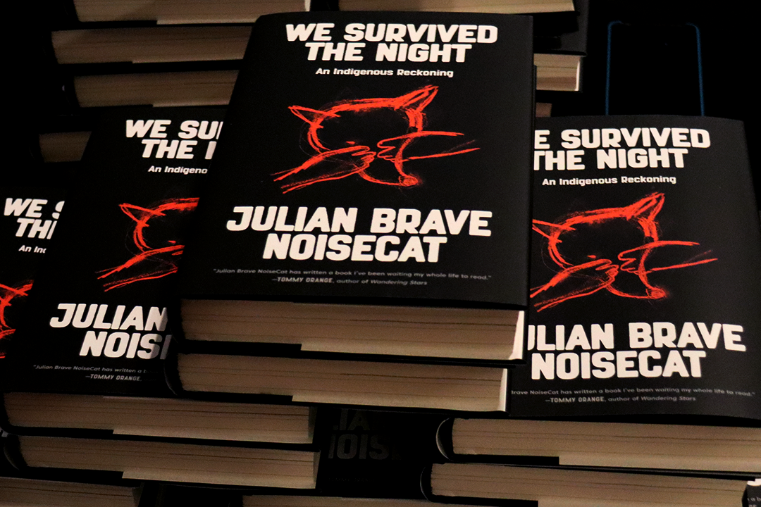 A stack of books. They are black with a red coyote on the front. The title says "We Survived the Night" and the author is Julian Brave NoiseCat.