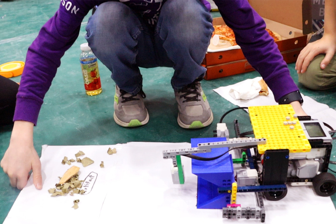 LEGO robot placed on a sheet of white paper, parallel to a pile of leaves and a drawn artifact.