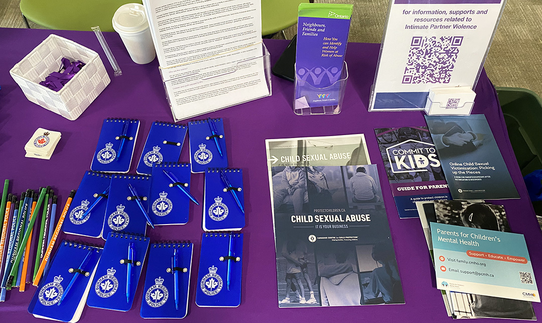 A table with a purple tablecloth has small DRPS notepads, pencils, stickers, informational pamphlets and cards.
