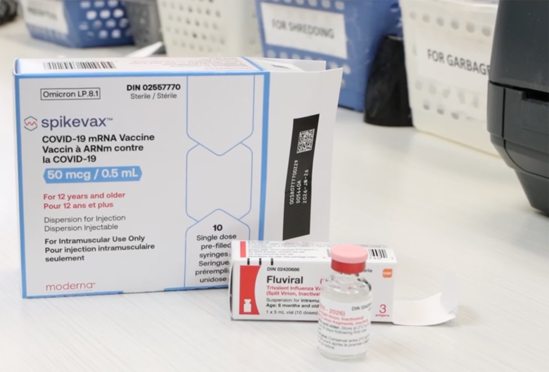 A white box that says 'spikevax' sits on a counter behind a clear vial with a red lid.